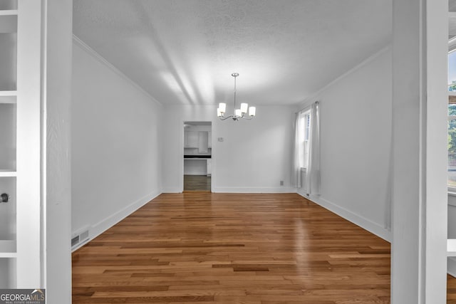 unfurnished dining area featuring visible vents, a chandelier, a textured ceiling, crown molding, and wood finished floors