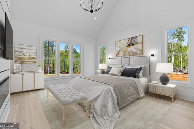 bedroom featuring high vaulted ceiling, multiple windows, a chandelier, and light wood-style floors