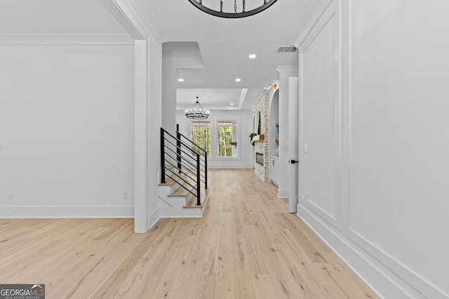 entryway featuring visible vents, light wood-type flooring, an inviting chandelier, and ornamental molding