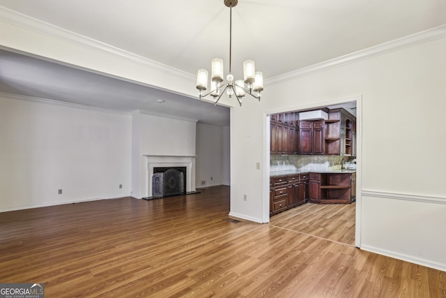 45 Willow Gln NE, Atlanta, GA 30342 - unfurnished living room with light wood-style floors, crown molding, an inviting chandelier, a fireplace with raised hearth, and baseboards