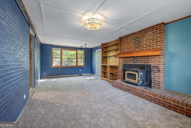 unfurnished living room with brick wall, carpet flooring, built in shelves, and a wood stove