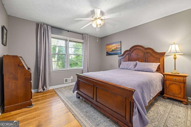 bedroom featuring light wood-style flooring, a textured ceiling, a ceiling fan, visible vents, and baseboards
