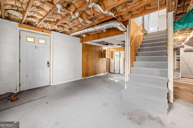 unfinished basement featuring stairs and concrete block wall