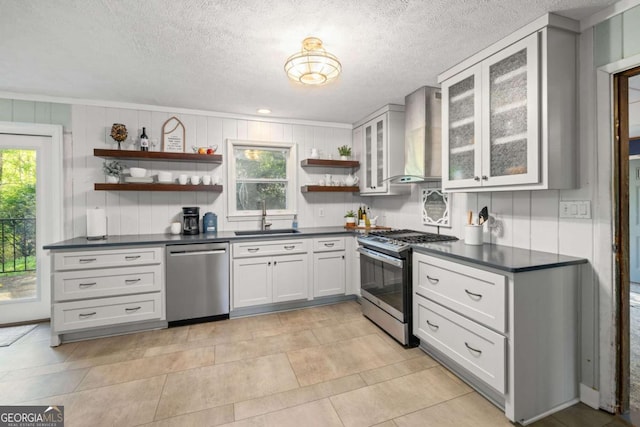 kitchen with open shelves, wall chimney exhaust hood, a sink, appliances with stainless steel finishes, and dark countertops
