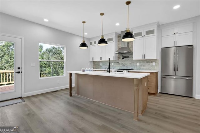 5719 Calm Valley Pt, Flowery Branch, GA 30542 - kitchen with stainless steel fridge, wall chimney exhaust hood, light countertops, decorative backsplash, and light wood finished floors