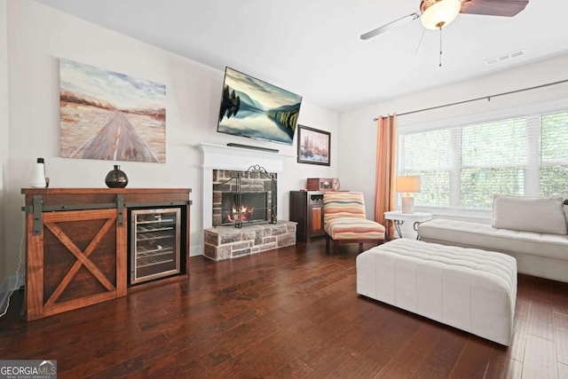 living room with ceiling fan, a stone fireplace, visible vents, wood finished floors, and beverage cooler
