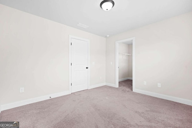 unfurnished bedroom with a walk in closet, carpet flooring, and baseboards