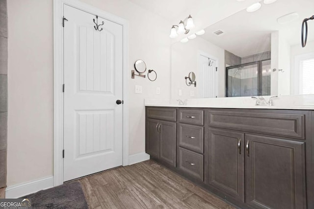 full bath featuring baseboards, double vanity, a stall shower, visible vents, and wood finished floors