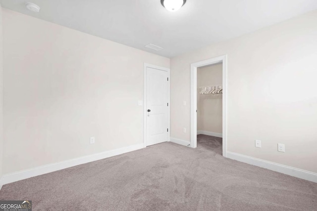 unfurnished bedroom featuring a closet, a walk in closet, carpet flooring, and baseboards