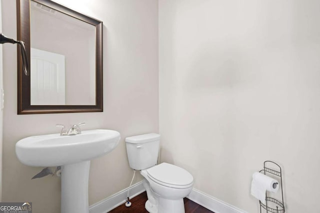 half bath featuring toilet, wood finished floors, and baseboards