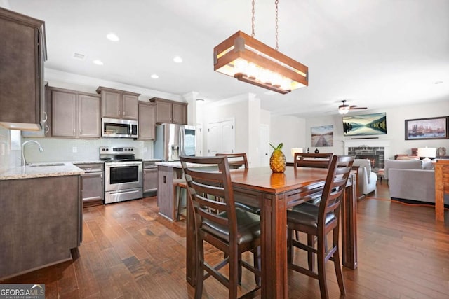 dining space with dark wood-style flooring, a warm lit fireplace, ceiling fan, crown molding, and recessed lighting