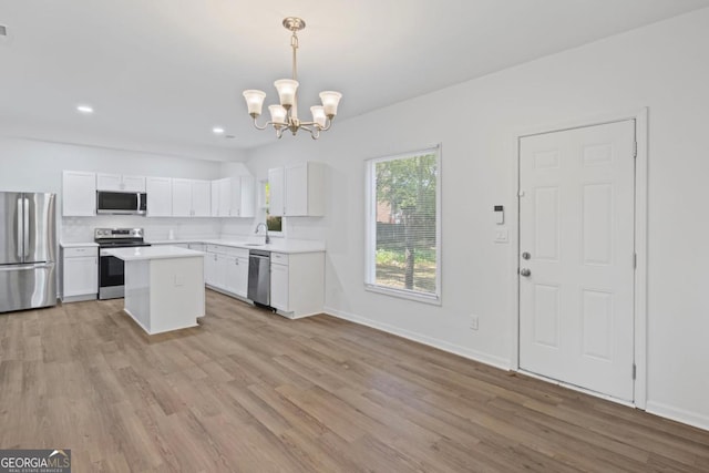 kitchen with white cabinets, appliances with stainless steel finishes, light countertops, a sink, and a notable chandelier