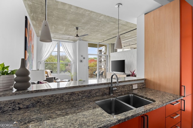 kitchen with hanging light fixtures, a sink, a ceiling fan, and dark stone counters
