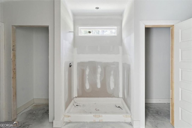 full bath with unfinished concrete floors, baseboards, and a stall shower