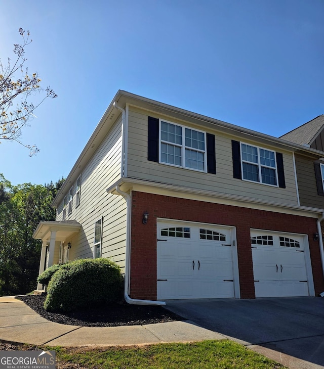 view of side of property with brick siding, an attached garage, and concrete driveway
