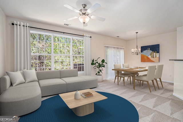carpeted living room with baseboards, visible vents, and ceiling fan with notable chandelier