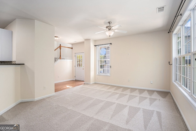 carpeted empty room with baseboards, a ceiling fan, and visible vents
