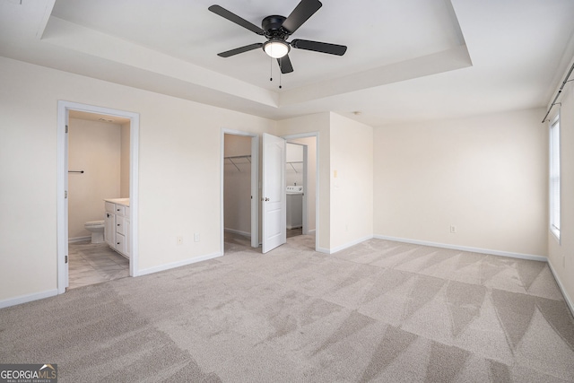 unfurnished bedroom featuring light carpet, washer / clothes dryer, baseboards, a tray ceiling, and a spacious closet
