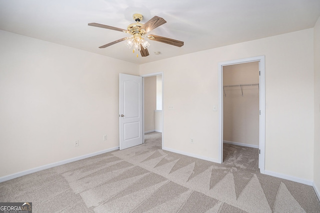 unfurnished bedroom featuring a walk in closet, ceiling fan, baseboards, a closet, and light carpet