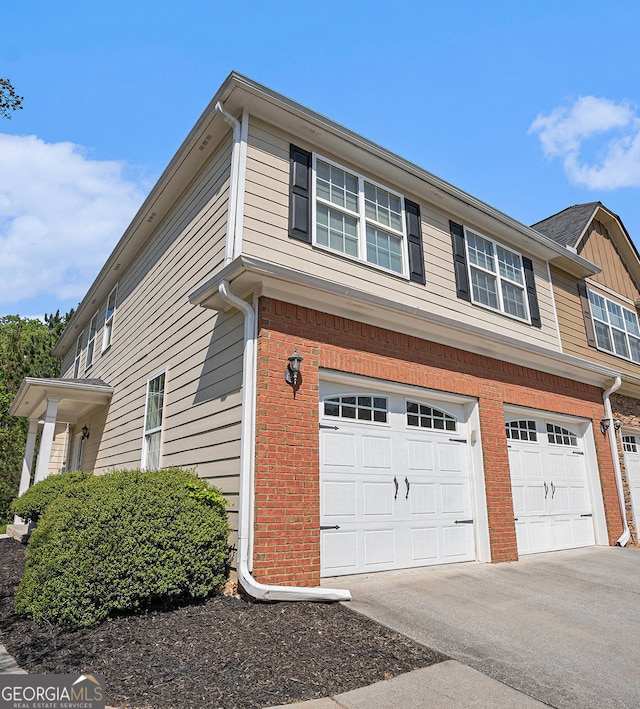 view of side of property with brick siding, an attached garage, and aphalt driveway