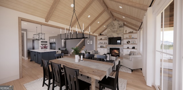 dining space featuring light wood-style floors, a stone fireplace, beam ceiling, and wood ceiling