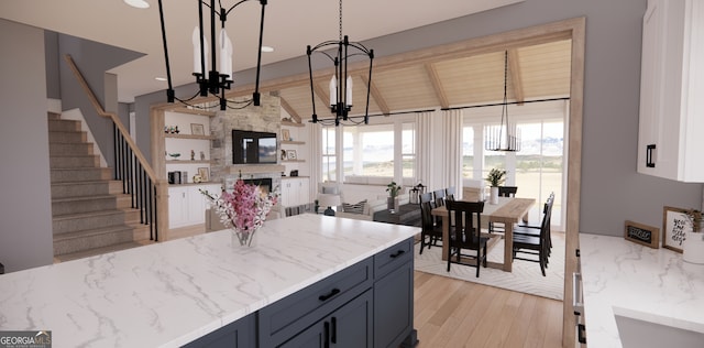 kitchen with vaulted ceiling with beams, light wood finished floors, a fireplace, a notable chandelier, and light stone countertops