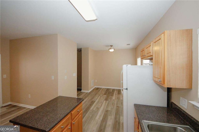 kitchen with a sink, light wood-style flooring, freestanding refrigerator, and baseboards