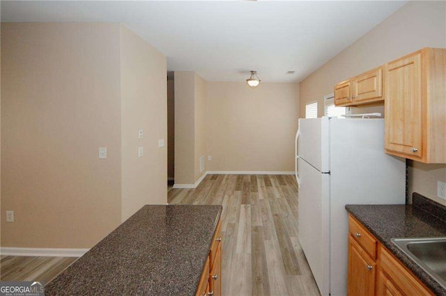 kitchen featuring a sink, light wood finished floors, baseboards, and freestanding refrigerator