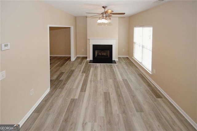 unfurnished living room with light wood-style flooring, ceiling fan, a fireplace with flush hearth, and baseboards