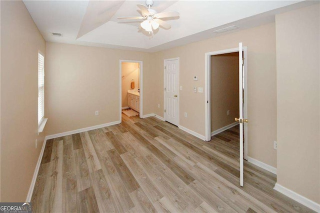 unfurnished bedroom with a tray ceiling, baseboards, light wood finished floors, and visible vents