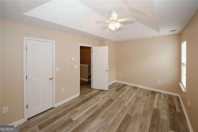 unfurnished bedroom with visible vents, baseboards, wood finished floors, and a raised ceiling