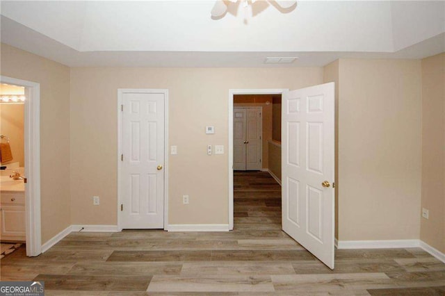 unfurnished bedroom with ensuite bathroom, baseboards, visible vents, and wood finished floors