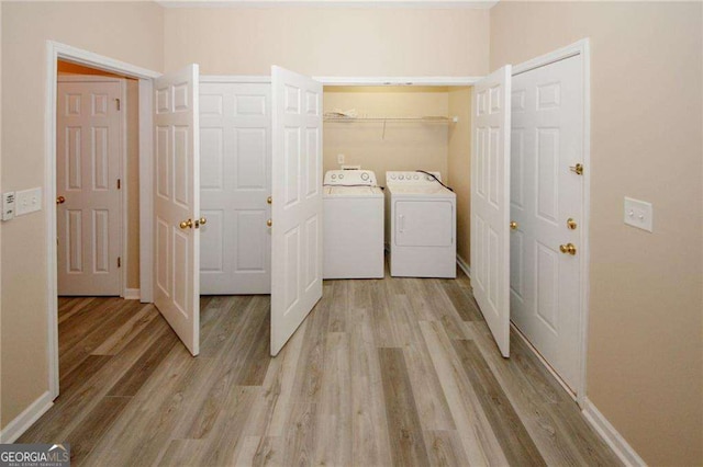 clothes washing area featuring laundry area, washing machine and clothes dryer, baseboards, and light wood-type flooring