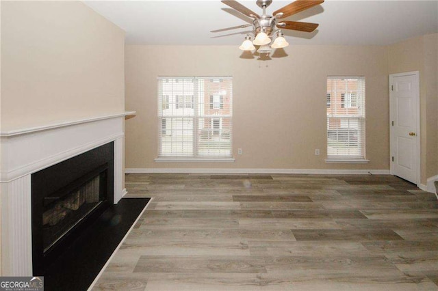 unfurnished living room with ceiling fan, wood finished floors, a fireplace with flush hearth, and baseboards