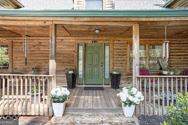view of exterior entry with roof with shingles and covered porch