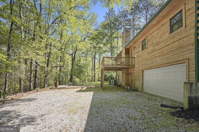 view of yard with an attached garage, central AC unit, and a wooden deck