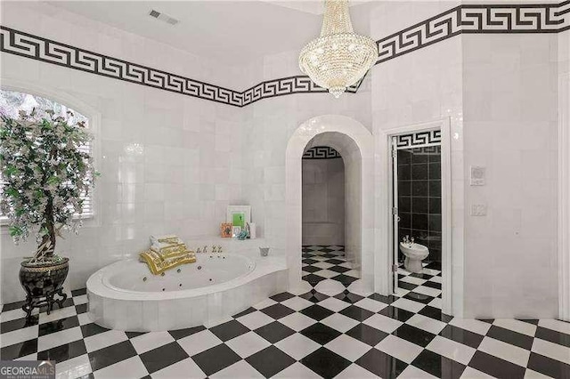 bathroom with tile patterned floors, an inviting chandelier, a tub with jets, and tile walls
