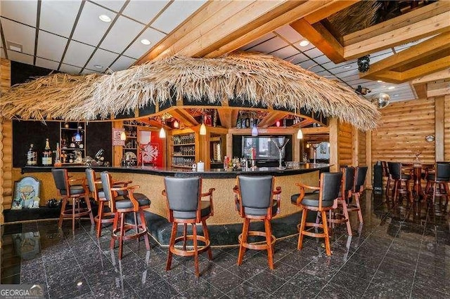 bar with a dry bar, a paneled ceiling, and log walls