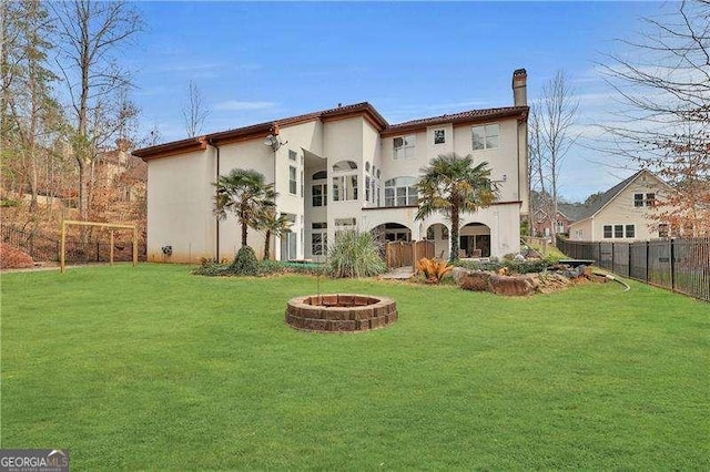 back of property featuring a fire pit, a yard, stucco siding, and fence