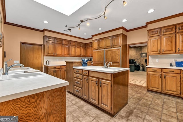 kitchen with a sink, brown cabinets, light countertops, ornamental molding, and an island with sink