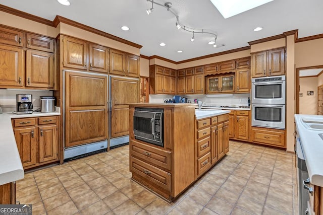 kitchen with black microwave, stainless steel double oven, ornamental molding, brown cabinetry, and light countertops