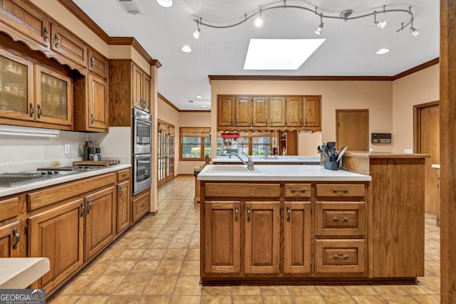 kitchen featuring a skylight, a sink, crown molding, brown cabinets, and a center island with sink