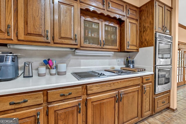 kitchen featuring double oven, stovetop with downdraft, brown cabinetry, and light countertops
