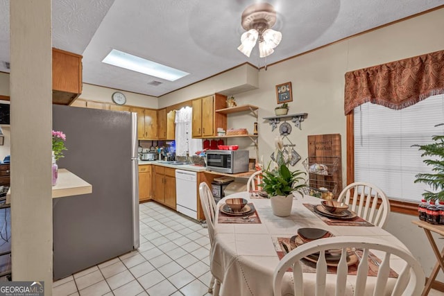 dining space with light tile patterned floors, a skylight, and a ceiling fan