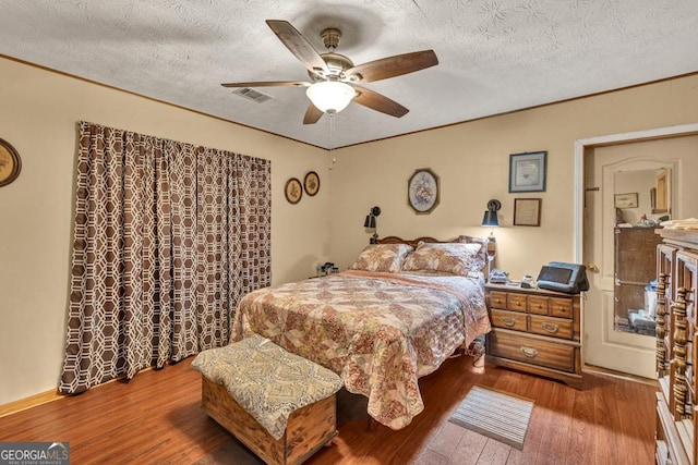 bedroom with a textured ceiling, hardwood / wood-style floors, crown molding, and a ceiling fan
