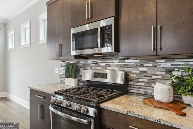 kitchen featuring dark brown cabinetry, crown molding, stainless steel appliances, backsplash, and light stone counters