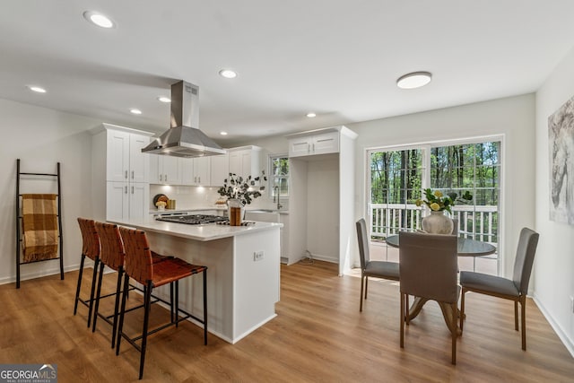 388 Pine Trl, Canton, GA 30115 - kitchen with light wood-style floors, decorative backsplash, white cabinetry, stainless steel gas cooktop, and island range hood
