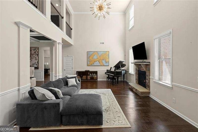 living room featuring baseboards, a notable chandelier, a fireplace, crown molding, and dark wood finished floors