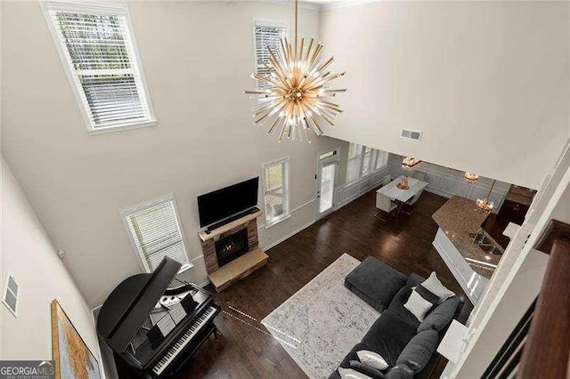 living room with a notable chandelier, a towering ceiling, a lit fireplace, visible vents, and wood finished floors