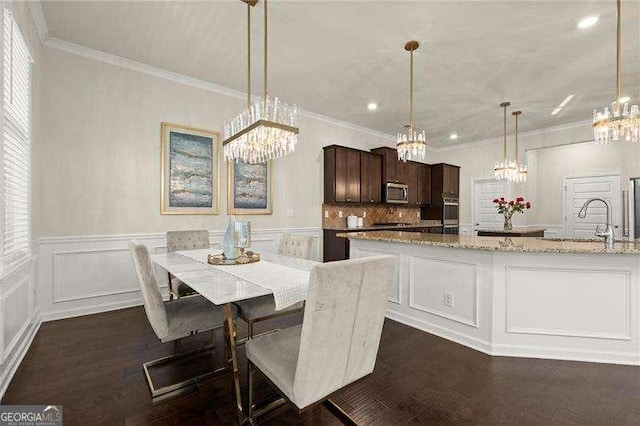 dining room featuring a decorative wall, dark wood-type flooring, a notable chandelier, and ornamental molding